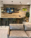 Home bar area with TV, shelves, and bar stools; warning sign "This Equipment Starts Automatically" on the wall.