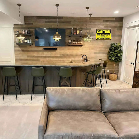 Home bar area with TV, shelves, and bar stools; warning sign "This Equipment Starts Automatically" on the wall.