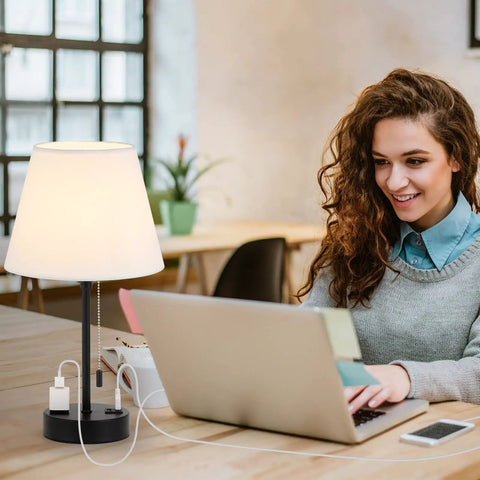 Set of 2 Modern Bedside Lamps With Ivory White Barrel Shade and Sleek Silver Metal Base on a desk with a woman using a laptop