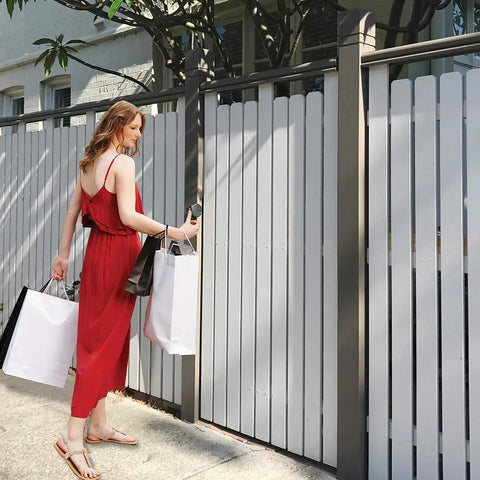 Woman in red dress with shopping bags near a white fenced gate, using Heavy Duty Adjustable Gate Latch With Six Pin Key Lock.