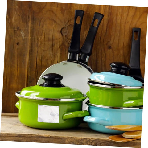 Green and blue enamel pots with lids and black-handled frying pans on wooden background