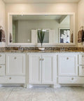 Bathroom vanity with large mirror, granite countertop, and white cabinet doors featuring crystal knobs, plant on counter.