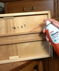 Hand holding Silicone Lubricant With Teflon Fluoro Polymer For Non Metal Materials near wooden drawer, demonstrating application.