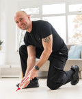Man using All In One Floor Repair Adhesive For Loose Hollow Tiles And Creaky Wood From A Simple Squeeze Tube With Precision Tip Drill And Fill No Mess Easy To Use For DIY And Pro Grade Installations Made In The USA Fix Floors Fast And Durable in a living room.