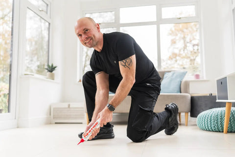 Man using All In One Floor Repair Adhesive For Loose Hollow Tiles And Creaky Wood From A Simple Squeeze Tube With Precision Tip Drill And Fill No Mess Easy To Use For DIY And Pro Grade Installations Made In The USA Fix Floors Fast And Durable in a living room.
