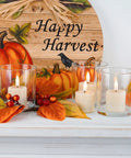 Flameless votive candles in glass holders on a mantle with fall decor and Happy Harvest sign