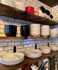 Badass Heavy Duty Metal Wall Shelf Brackets With Lip Slick Industrial Diy Floating Shelf Support System Black Anti Rust Finish Straight Up Reliable Mounting Hardware 2 Pack supporting kitchen plates and bowls in a rustic setting.