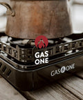 Close-up of a pot on a 15,000 BTU Dual Fuel Portable Camping Stove For Propane Or Butane, outdoor cooking gear on wood surface.