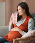 Celebrate The Freshly Minted Arrival Of New Mama And Papa With This Awesome Gift Set For Couples Featuring Matching Tumblers Paired With A Warm Cozy Candle Perfect For Baby Showers First Fathers Day And Parenting Squad Celebrations. Pregnant woman smiling while holding a pink insulated tumbler.