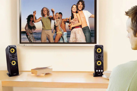 Man watching LCD TV with GigaWorks T40 Series II 2.0 Desktop Speaker System With BasXPort Tech Delivers Full Bass Without a Sub