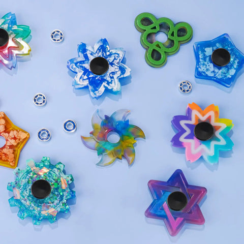 Colorful DIY fidget spinners with Fidget Spinner Bearings With Caps 24 Pack Chrome Steel Craft Set arranged on a blue surface.