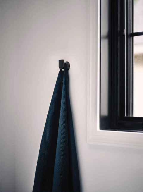 Genta LX Modern Single Robe Hook And Towel Hanger In Matte Black near window holding dark towel, space-saving bathroom accessory BH3803BL