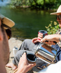 Pouring coffee from 3 Cup Percolator Coffee Pot In Glacier Stainless Steel With Silicone Handle For Camping near a river