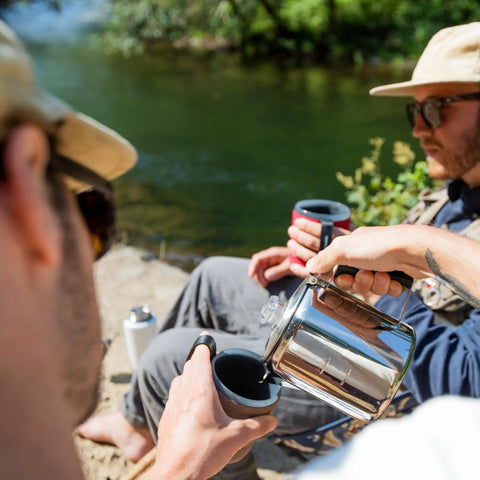 Pouring coffee from 3 Cup Percolator Coffee Pot In Glacier Stainless Steel With Silicone Handle For Camping near a river