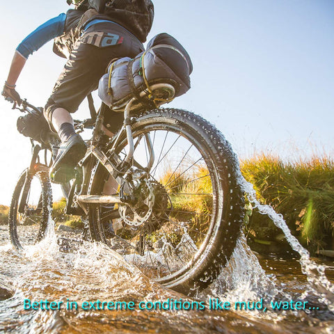 Side view of two mountain bikes with disc brakes riding through water; outdoor gear and packs visible.