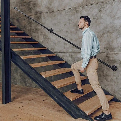Man ascending stairs using Adjustable Step Handrail For Indoor Outdoor Stairs, Heavy Duty Wrought Iron Wall Banister, No Sweat Install For Seniors And Families, Top Shelf Black Finish.