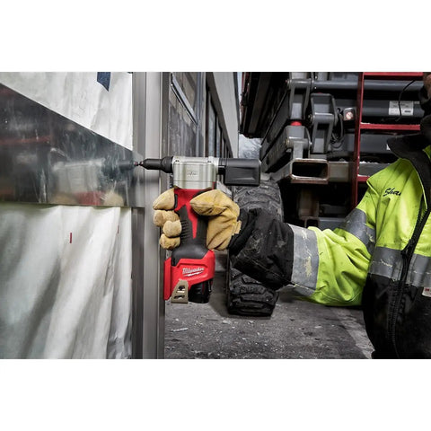 Milwaukee M12 Cordless Rivet Tool Bare Unit held by a worker in gloves, fastening metal, showcasing lightweight design.