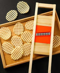 Wave waffle crinkle cutter set with wooden frame and metal blade; round lattice-cut potato chips on tray.
