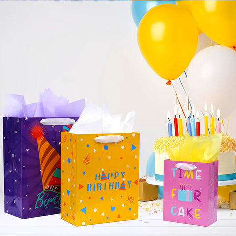 Three birthday gift bags with ribbon handles and tissue paper, assorted sizes including extra large, large, and medium