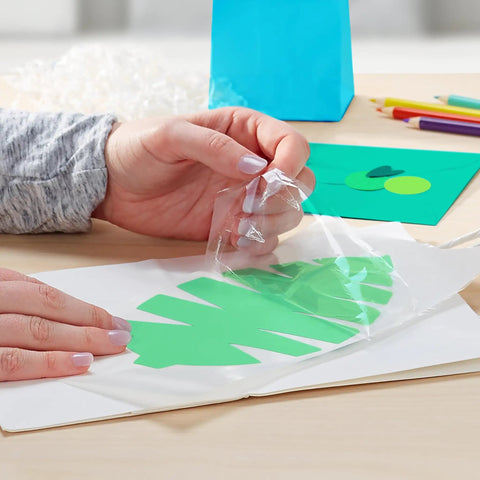 Using Big League Permanent Adhesive Refill Cartridge to apply a green leaf cutout on white paper for crafting.