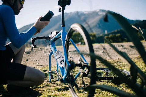 Cyclist holding 0.8L Waterproof Bike Tool Capsule For Bottle Cages Screw Cap Seal beside a road bike with mountain backdrop