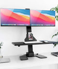 Electric Dual Monitor Sit Stand Desk Converter with 28 Inch Base Height Adjustable Desktop Riser holding two 32-inch screens