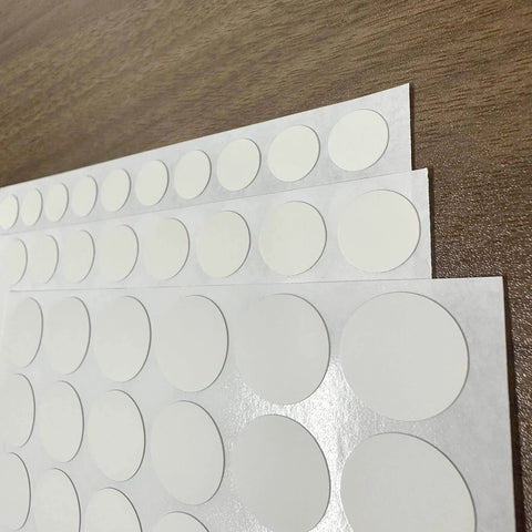White Screw Hole Cover Set Including 290 Pieces In Three Sizes 12mm 15mm And 21mm Self Adhesive PVC Caps on a wooden surface