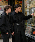 Premium Industrial Steel Punk Metal Belt In Matte Black With Easy Hook And Loop Sizing For Badass Gothic Streetwear Fits, worn by two young men browsing vinyl records.