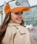 Woman wearing an orange and white cap with text, enjoying a day out. Unisex Adjustable Sun Hat Cap For Men And Women Breathable All Day Comfort Versatile Outdoor Gear For Boat Days Beach Hangouts And Casual Sportswear With Dope Athletic Inspired Style.