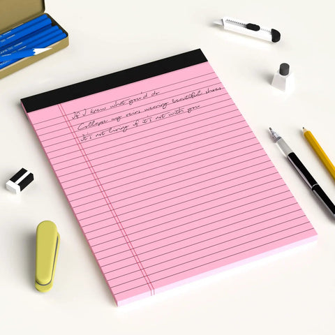 Pink Legal Pad 8.5 X 11 Wide Ruled Writing Pad Set With Perforated Backing 30 Sheets Per Pad on a desk with pens and clips