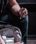 Person holding ProTac 1L-1AA 350-Lumen Compact Tactical LED Flashlight With Alkaline Battery Coyote Finish near open backpack.