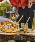 14 Inch Perforated Pizza Peel With Long Handle Aluminum Lightweight Pizza Paddle holding a pizza on an outdoor table
