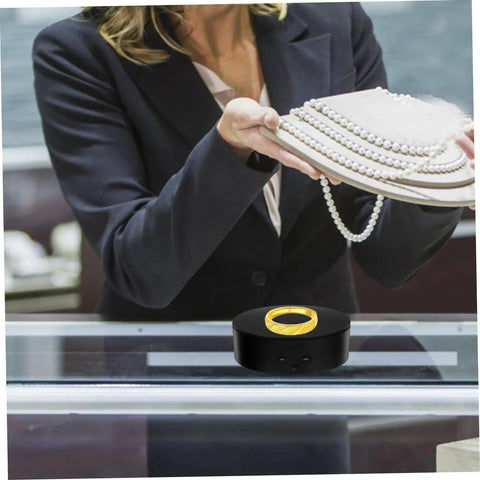 Compact Electric Rotating Turntable Stand For Jewelry Display on a counter, showcasing a gold ring with pearl necklaces.
