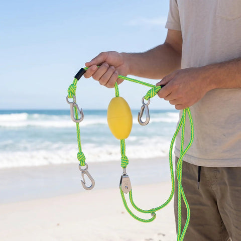 Person holding a Marine Tow Line With Pulley Shock Absorb Bungee Dock Line Stretchable Rope in yellow and green on a beach