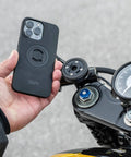 Person holding phone near SPC Plus Anti Vibration Module on motorcycle, showing mounting position and screws.