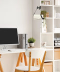 Modern office desk with computer, chair, white shelves, and decorative plants in a well-organized workspace.