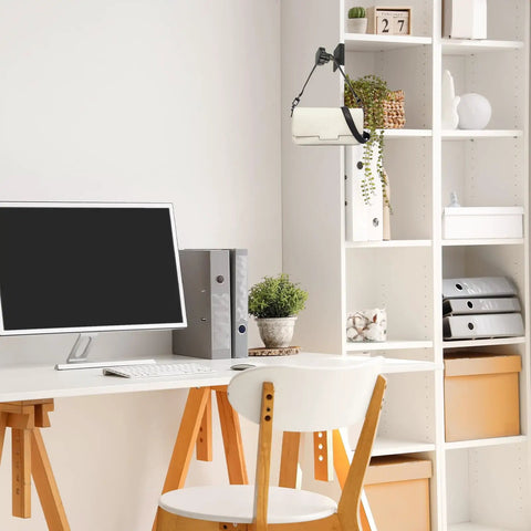 Modern office desk with computer, chair, white shelves, and decorative plants in a well-organized workspace.