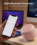 Hand holding phone showing Bluetooth pairing with Ultra Portable Bluetooth Speaker With Strap For On The Go IPX5 Waterproof Mini Speaker That Bangs With Loud Stereo Sound 20 Hours Of Playtime Rechargeable Battery Built In Microphone Pink on table.