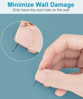Hand inserting tiny pin into wall with minimal damage, showcasing Solid As A Rock 10 Piece Heavy Duty Picture Hangers And Frame Hooks Supporting Up To 100 Pounds For Mirrors Clocks Wall Art With Stealth Mounting Nails That Keep Your Drywall Looking Crisp Zero Hassle Guaranteed.