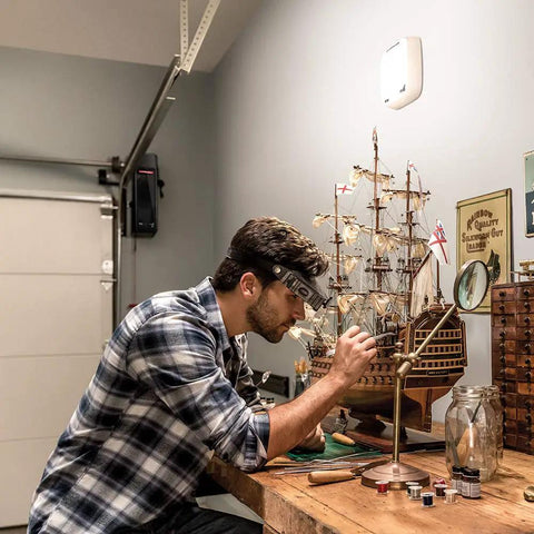 Man working on model ship in garage with Bright 1500 Lumen LED Light You Can Control And Schedule From Your Phone With A Smart Garage Hub Or Wi Fi Opener Super Easy Plug In No Tools Required For A Quick Garage Or Home Lighting Upgrade mounted on wall.
