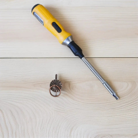 Screwdriver next to 80 Piece Retro Mini Cabinet Pull Handles Rings With Drop Bail Knobs For Small Furniture on wood surface.