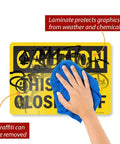 Hand wiping graffiti from Caution This Area Blocked Off Sign 10x14 Aluminum Black On Yellow Durable 40 Mil Outdoor Sign