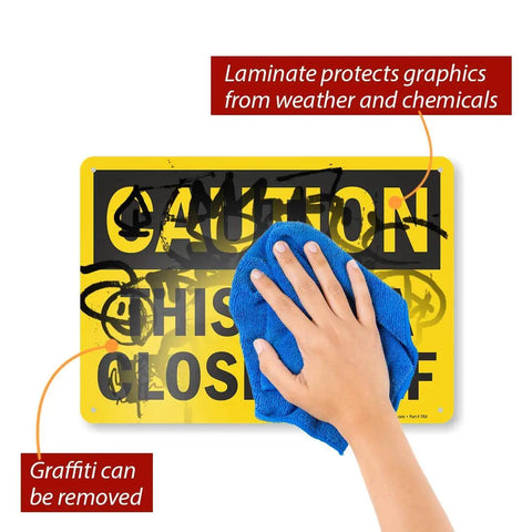 Hand wiping graffiti from Caution This Area Blocked Off Sign 10x14 Aluminum Black On Yellow Durable 40 Mil Outdoor Sign