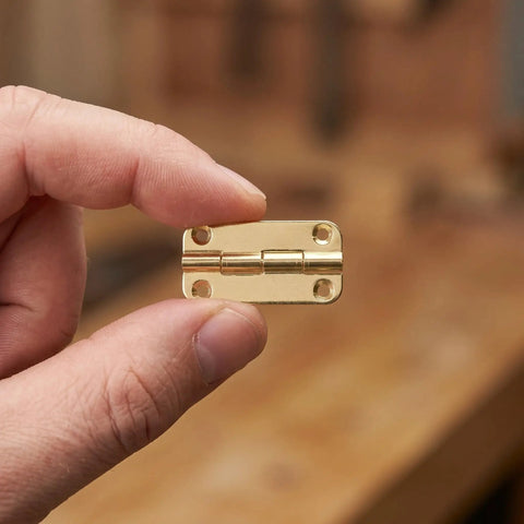 Person holding a gold hinge from the 12 piece mini antique iron folding cabinet hinges with rounded corners for cupboard doors and small boxes.