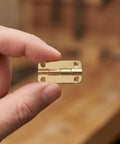 Close-up of hand holding one hinge from the 12 Piece Small Antique Iron Cabinet Hinges Set With Rounded Corners Four Hole Vertical Mount