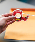 Person using Super Hold Tape With 50 Percent More Adhesive, Clear Finish, 2 Rolls, Dispenser Ready over an envelope on a table.