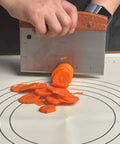 Person using Heavy Duty Bench Scraper For Flat Top Griddle, Dough Cutter And Bread Pizza Scraper to slice carrots on a board.