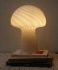 Mushroom Glass Table Lamp 12.75 Inch For Bedside Tables And Desks, glowing warmly on books with subtle glass twist design.
