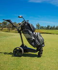Slick Remote Controlled Electric Golf Push Cart Bundle With Top Shelf Touchscreen Gps Navigation And Preloaded Courses For Thirty Six Holes With Built In Drink Holder And Compact Umbrella Mount Plus Badass Travel Carry Bag on green golf course.
