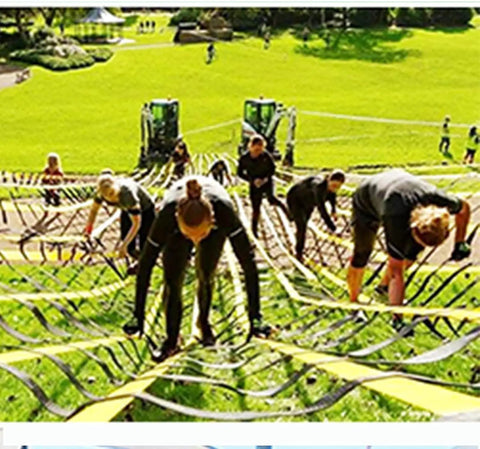 People climbing over obstacle course using ropes and nets in an outdoor setting with greenery in the background